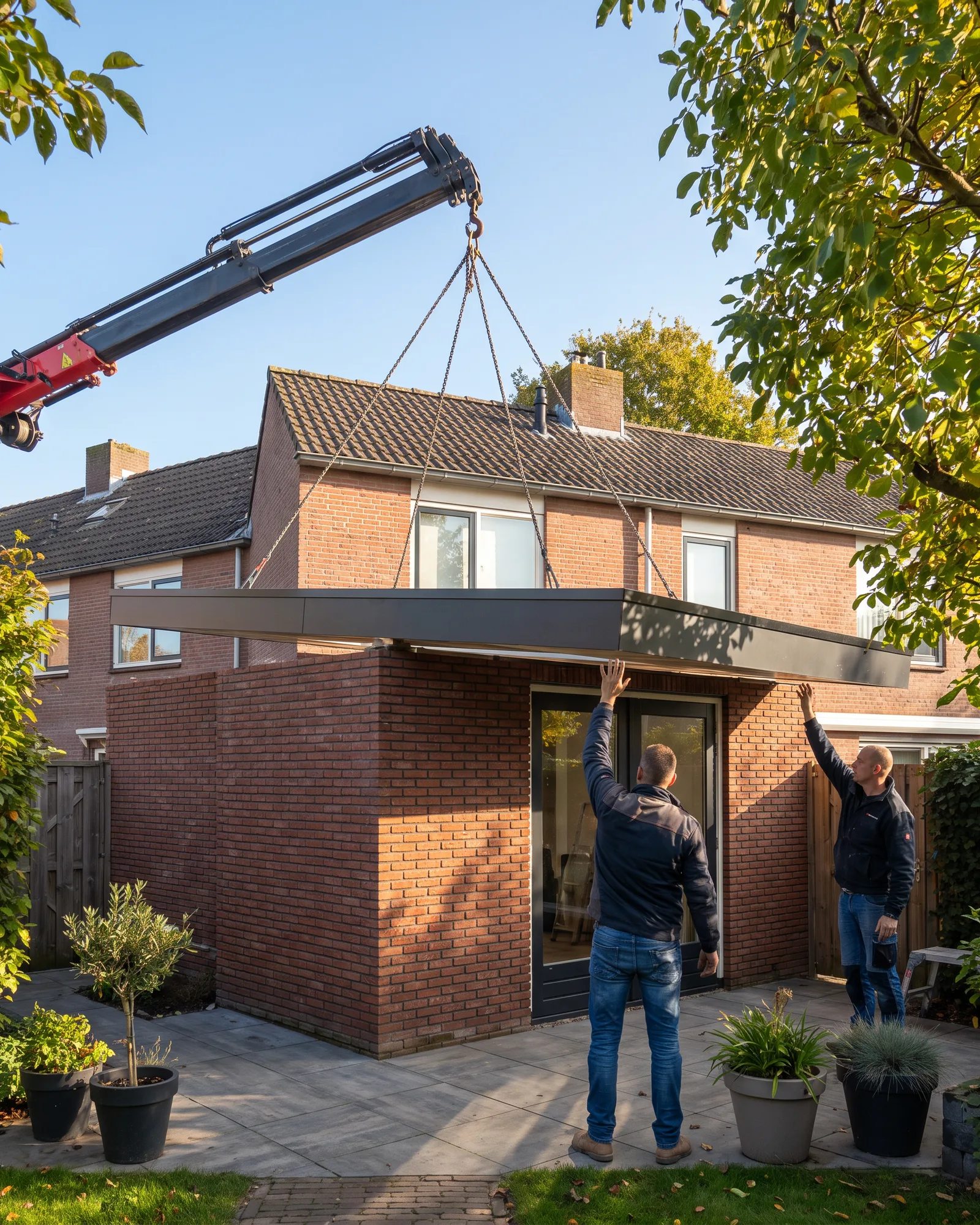 Een kraan zet een prefab dakdeel op een nieuwe uitbouw aan een rijwoning, in de zon
