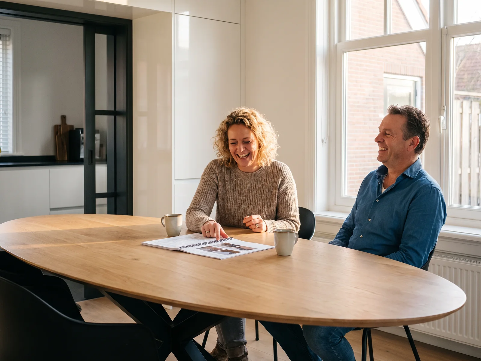 Een eigenaar en onze adviseur ontspannen in gesprek aan een lange tafel, met het rapport tussen hen in
