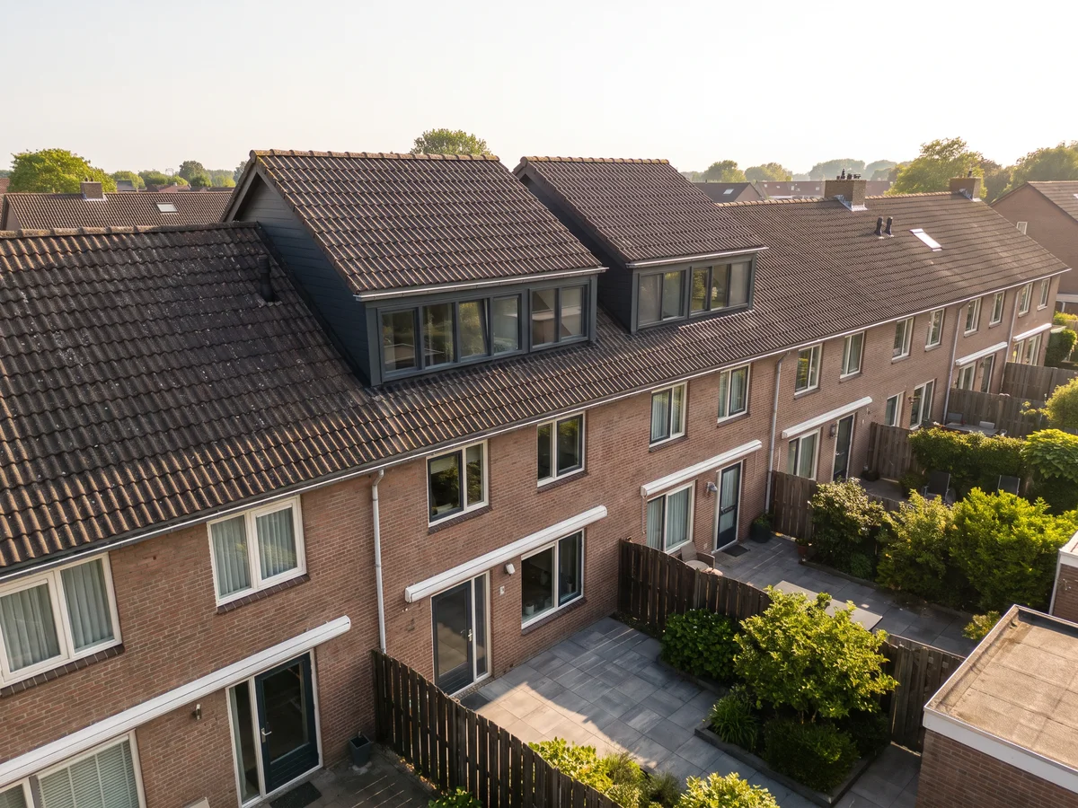 De achterkant van een rij woningen, waarvan twee met een hoger opgetrokken dak en een strook ramen