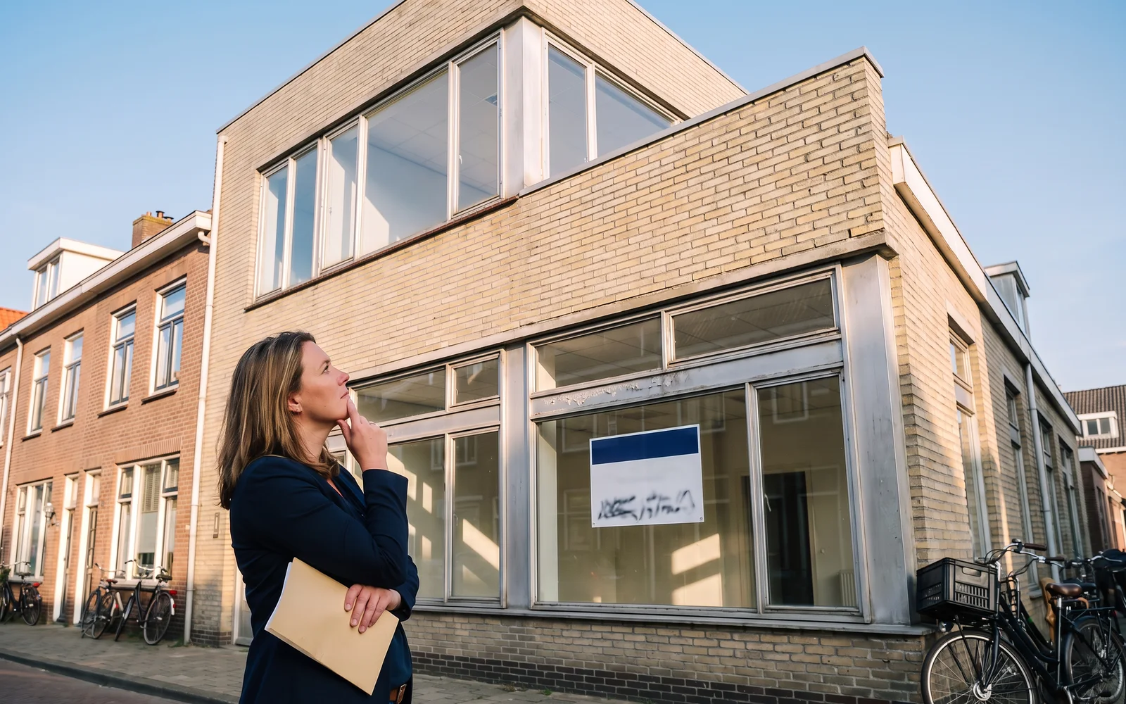 Een leeg kantoorpand in een Nederlandse straat, in de zon, dat tot woningen verbouwd kan worden