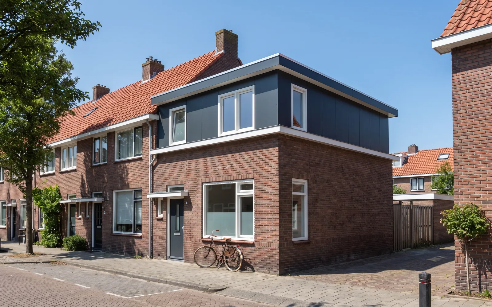 Een rijwoning met een nieuwe dakopbouw met strakke witte kozijnen, in de middagzon